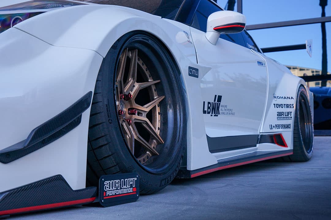 A white vehicle lowered with Air Lift Performance at a car show.